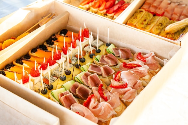 Aperitivos gourmet en caja de cartón con bocadillos, canutillos, bruschetta con fiambres, quesos y mariscos para catering buffet y fiesta.