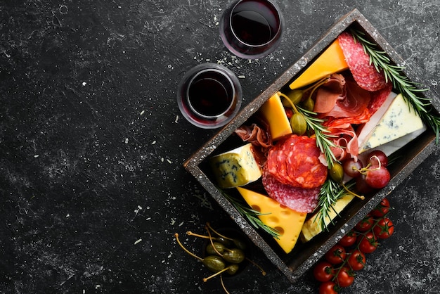 Aperitivos italianos Queso, vino, salami y prosciutto sobre un fondo de piedra negra Vista superior Espacio libre para el texto