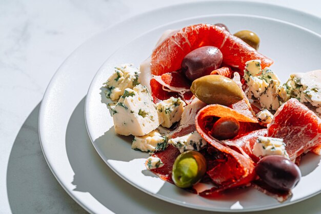 Aperitivos italianos tradicionales jamón aceitunas y queso azul jamón picado con una variedad de aceitunas en escabeche y trozos de queso azul caro junto a una copa de vino fresco