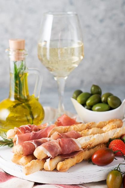 Aperitivos italianos tradicionales para vino, palitos de pan (grissini), tomates, prosciutto (jamón), fresas y aceitunas. Enfoque selectivo, de cerca