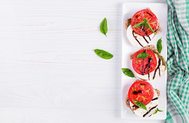 Aperitivos con mozzarella, tomate y pan de centeno en la mesa de madera blanca. Vista superior