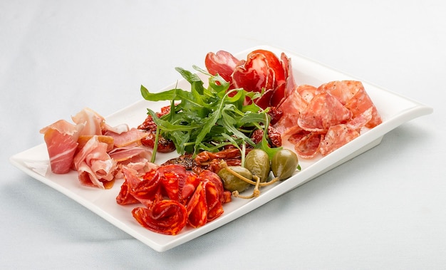 Aperitivos de salchichas italianas Prosciutto chorizo pancetta y salami Alcaparras rúcula y tomates secos Sobre fondo blanco