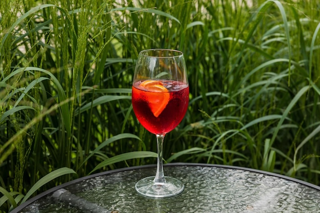 Aperol spritz aperitivo refrescante coquetel alcoólico em uma taça de vinho do lado de fora em uma mesa de vidro no alto da grama verde no espaço de cópia bokeh