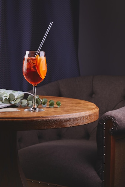 Aperol-Spritz-Cocktail mit Eis im Glas auf Holztisch im dunklen Innenraum