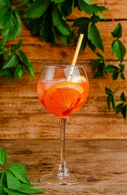 Aperol Spritz Cocktail mit Trinkhalm auf rustikalem Holzhintergrund.