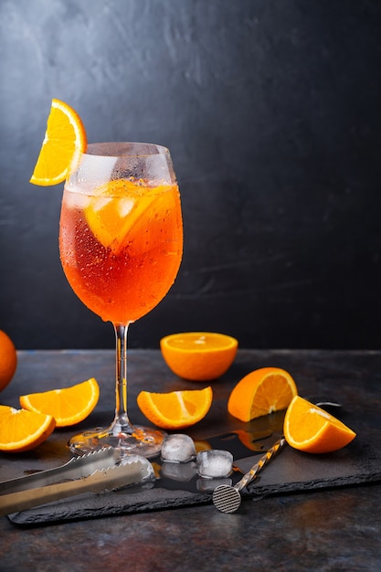 Aperol spritz cocktail- und barzubehör. italienischer aperol-spritz-cocktail und eine in scheiben geschnittene orange auf dunklem hintergrund. sommercocktail aperol spritz auf einer schiefertafel