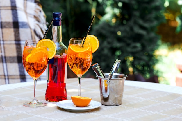 Aperol spritz mesa de vidro xadrez folhas sol sol laranja balde de gelo sombra luz solar