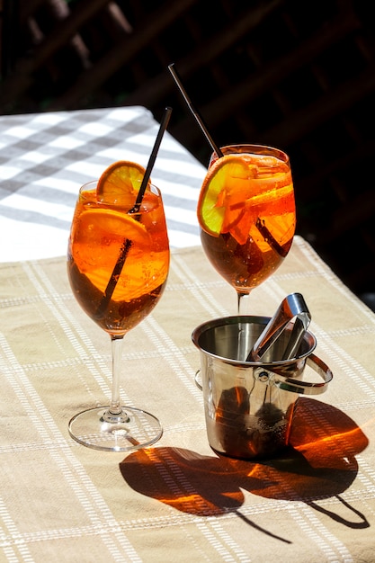 Aperol spritz mesa de vidro xadrez folhas sol sol laranja balde de gelo sombra luz solar