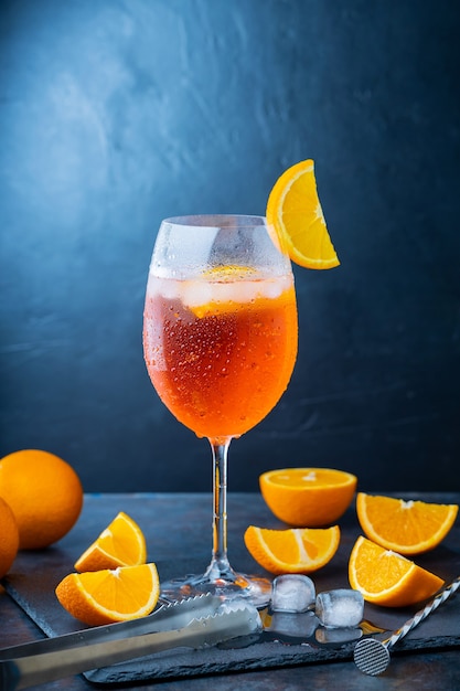 Aperol spritz para coquetéis e acessórios para bar. Coquetel de aperol italiano e uma laranja em fatias em um fundo escuro. Coquetel de verão com spritz de aperol em ardósia