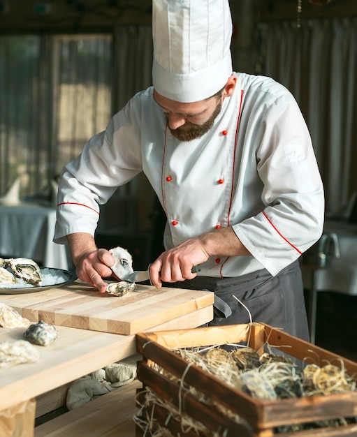 Apertura de las ostras huecas y planas. Chef abre las ostras en el restaurante.