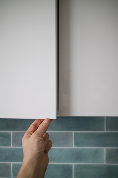 Apertura de la puerta del armario de cocina sin tirador con foco en la acción de apertura de la mano masculina. Diseño de muebles modernos sin manija de puerta y cerraduras.