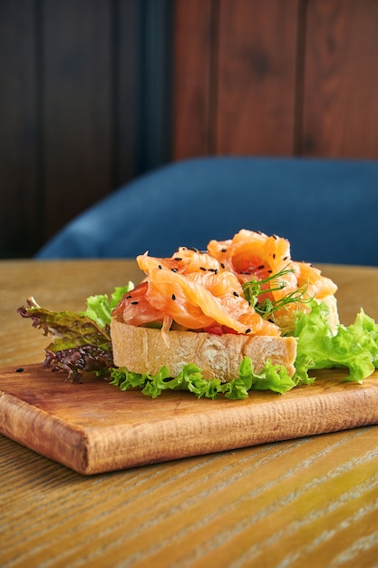 Apetitosa bruschetta con salmón y lechuga en una tabla de cortar en una pared de madera. Primer plano, enfoque selectivo