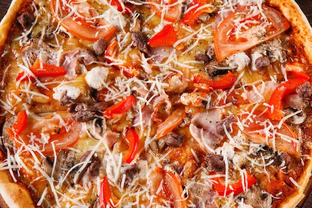 Apetitosa y deliciosa pizza colorida recién horneada con champiñones, tocino, pollo, pimentón y tomate, de cerca. Cocina italiana, comida rápida tradicional.