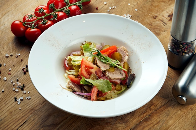 Apetitosa ensalada caliente con carne y verduras frescas en un plato blanco sobre madera.