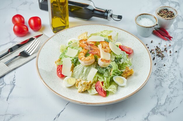 Apetitosa ensalada César con camarones, picatostes, parmesano, tomates y salsa de anchoas en un plato blanco sobre una superficie de mármol