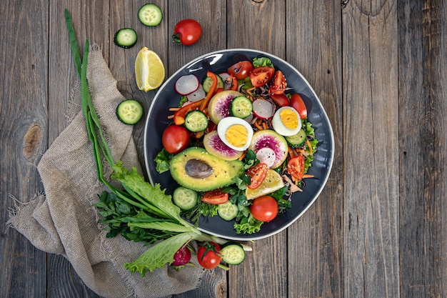 Apetitosa ensalada de verduras con aguacate de huevos sobre un fondo de madera