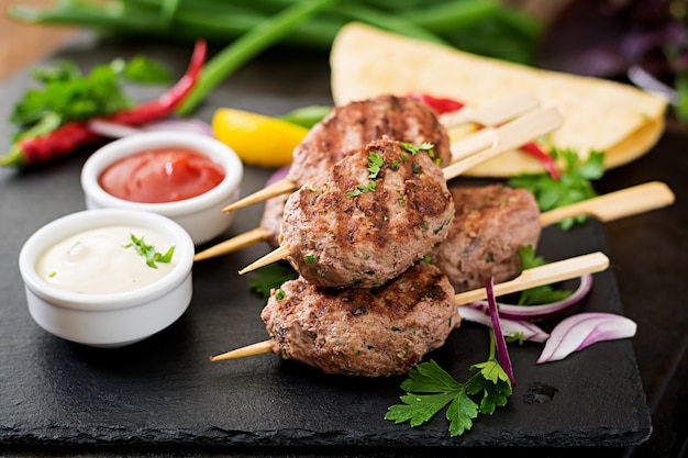 Apetitosa kofta kebab (albóndigas) con tacos de salsa y tortillas sobre fondo negro