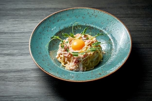 Apetitosa massa italiana carbonara com gema, molho branco e bacon em prato azul sobre fundo de madeira