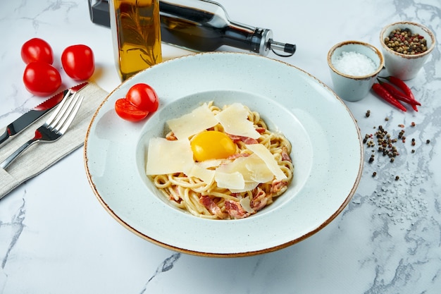 Apetitosa pasta carbonara italiana con salsa blanca, yema, tocino y queso parmesano en una placa blanca sobre una superficie de mármol