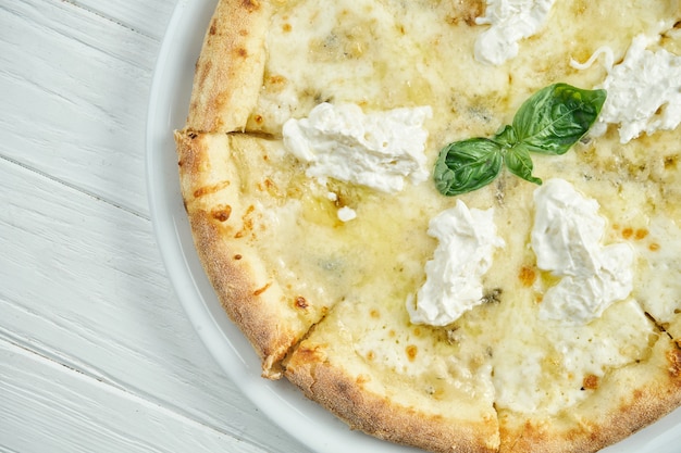 Apetitosa, pizza caseira de 4 queijos com queijo azul, mussarela, parmesão e strachatella em um prato branco sobre um branco