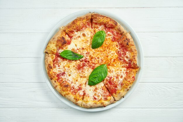 Apetitosa pizza casera con margarita con tomate, albahaca y mozzarella en un plato blanco sobre un blanco