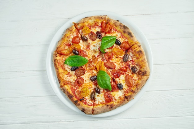 Apetitosa pizza casera con margarita con tomates cherry, albahaca y mozzarella sobre un blanco