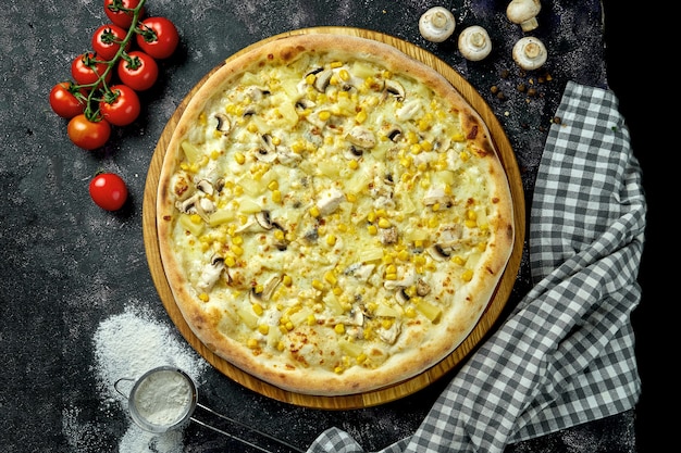 Foto apetitosa pizza havaiana com frango, cogumelos, milho e abacaxi em uma composição com ingredientes em uma mesa preta