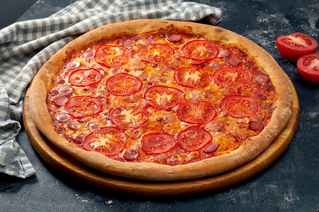 Apetitosa pizza con salchichas de leche, salsa roja, tomates y queso. Superficie oscura. Cocina italiana