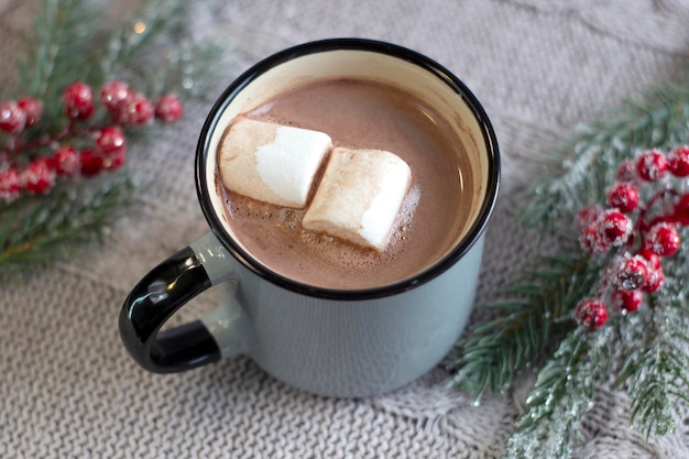 Apetitosa taza fragante de cacao con malvaviscos sobre un fondo de punto acogedor con una ramita de navidad