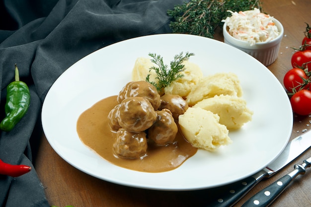 Apetitosas albóndigas de pollo en salsa con guarnición de puré de papas en un plato blanco sobre una mesa de madera en una composición con ingredientes