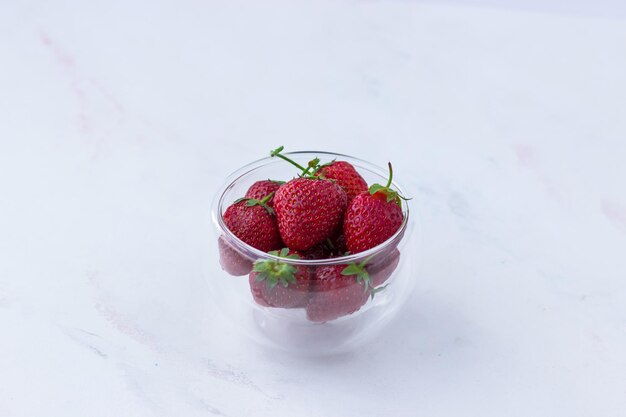 Apetitosas fresas en un jarrón transparente sobre un fondo blanco.