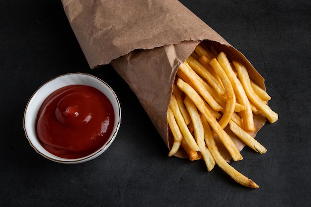 Apetitosas papas fritas crujientes en una bolsa de papel ecológica sobre un fondo negro Comida rápida americana caliente