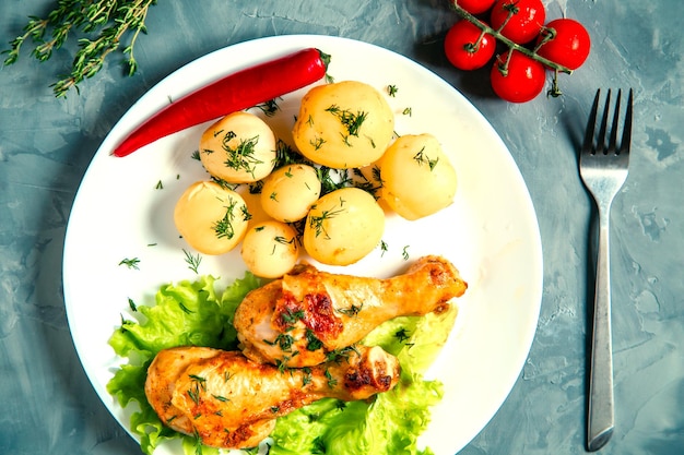 Apetitosas pernas de frango frito com batatas e vegetais novos.