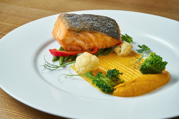 Apetitoso bife de salmão grelhado com um prato de purê amarelo, aspargos frescos, brócolis e couve-flor em um prato branco. Comida saudável e saborosa