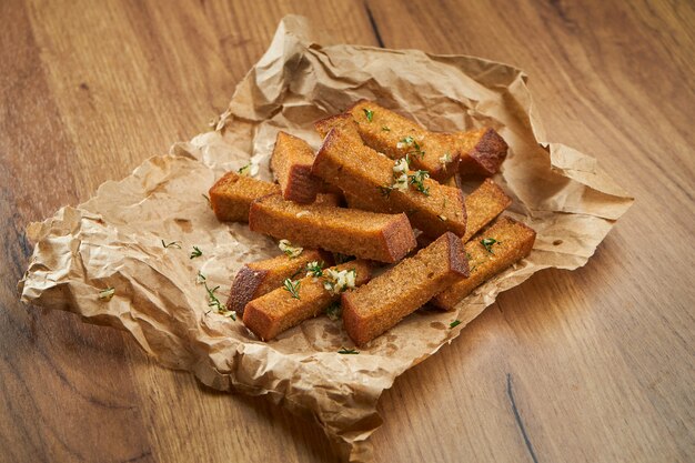 Apetitoso bocadillo con cerveza - picatostes de centeno con ajo y hierbas en pergamino sobre una superficie de madera.