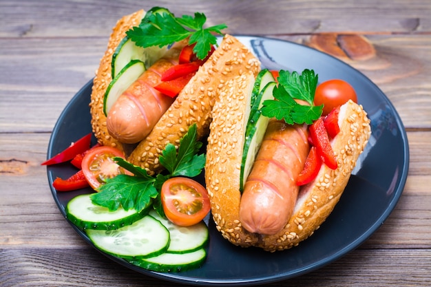 Apetitoso cachorro-quente de salsichas fritas, pão de gergelim e legumes frescos em um prato sobre uma mesa de madeira