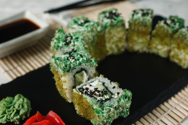 Apetitoso conjunto delicioso de rolos de sushi servido em ardósia preta, fundo de esteira de palha, closeup. Cozinha nacional japonesa, arte culinária.