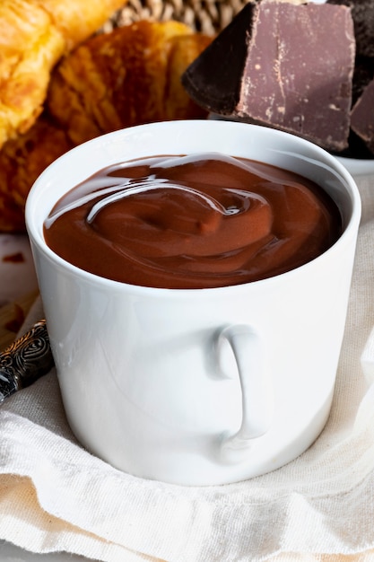 Foto apetitoso desayuno con una deliciosa taza de chocolate caliente espeso y bebible, junto con croissants.