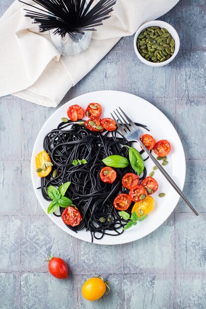 Apetitoso espaguete preto com tomates secos, sementes de abóbora e sementes de gergelim em um prato branco sobre a mesa. Comida gourmet. Vista superior e vertical