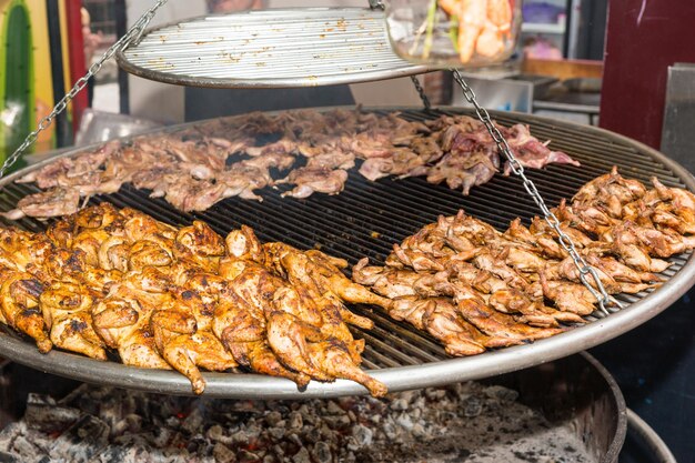 Apetitoso frango assado marinado ou carne de codorna na grelha quente no festival de comida, conceito de comida e bebida