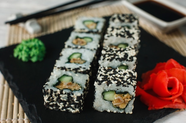 Apetitoso y fresco juego de rollos de uramaki con sésamo servido en pizarra negra, primer plano. Comida sana japonesa, sushi, mariscos.