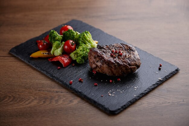 Apetitoso y jugoso filete de carne con especias y una guarnición en un plato de piedra sobre una mesa de madera.