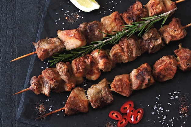 Apetitoso kebab con especias, chile y lima. Brochetas de cerdo fragantes en un tablero de piedra.