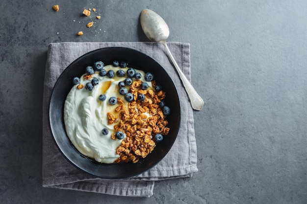 Apetitoso muesli casero con bayas y yogur servido en un tazón sobre fondo oscuro.