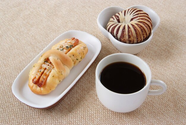 Apetitoso pan de taro de salchicha y una taza de café sobre un fondo de tela