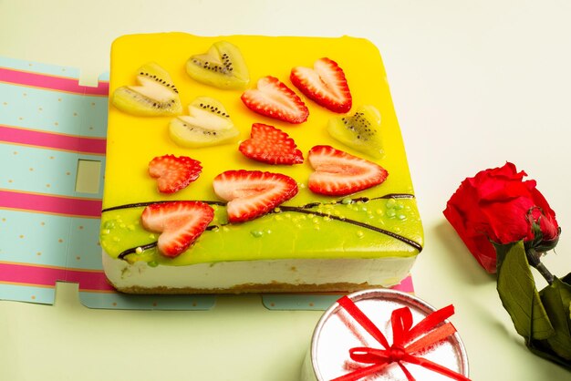 Apetitoso pastel cubierto de glaseado, decorado con corazones de fresas y piezas de kiwi con una rosa y una caja de regalo sobre un fondo claro, enfoque selectivo. Tarjeta de felicitación. Pastel para el día de San Valentín.