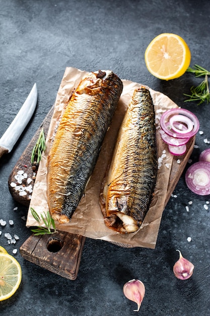 Apetitoso peixe defumado com especiarias, pimenta e legumes em papel ofício sobre fundo escuro de pedra. Comida mediterrânea, peixe arenque, frutos do mar, vista de cima