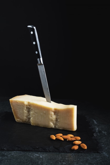 Un apetitoso queso sólido en un plato negro con cuchillo y almendras