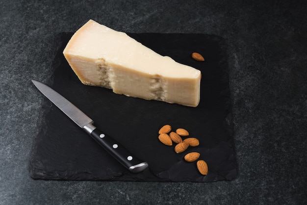 Foto un apetitoso queso sólido en un plato negro con cuchillo y almendras