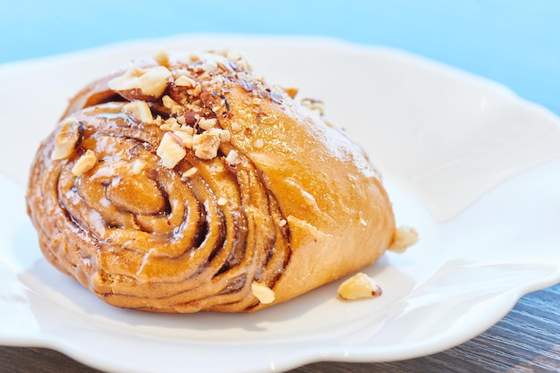 Apetitoso rollo de canela en un plato blanco. Pastelería casera, bollo con topping de nueces